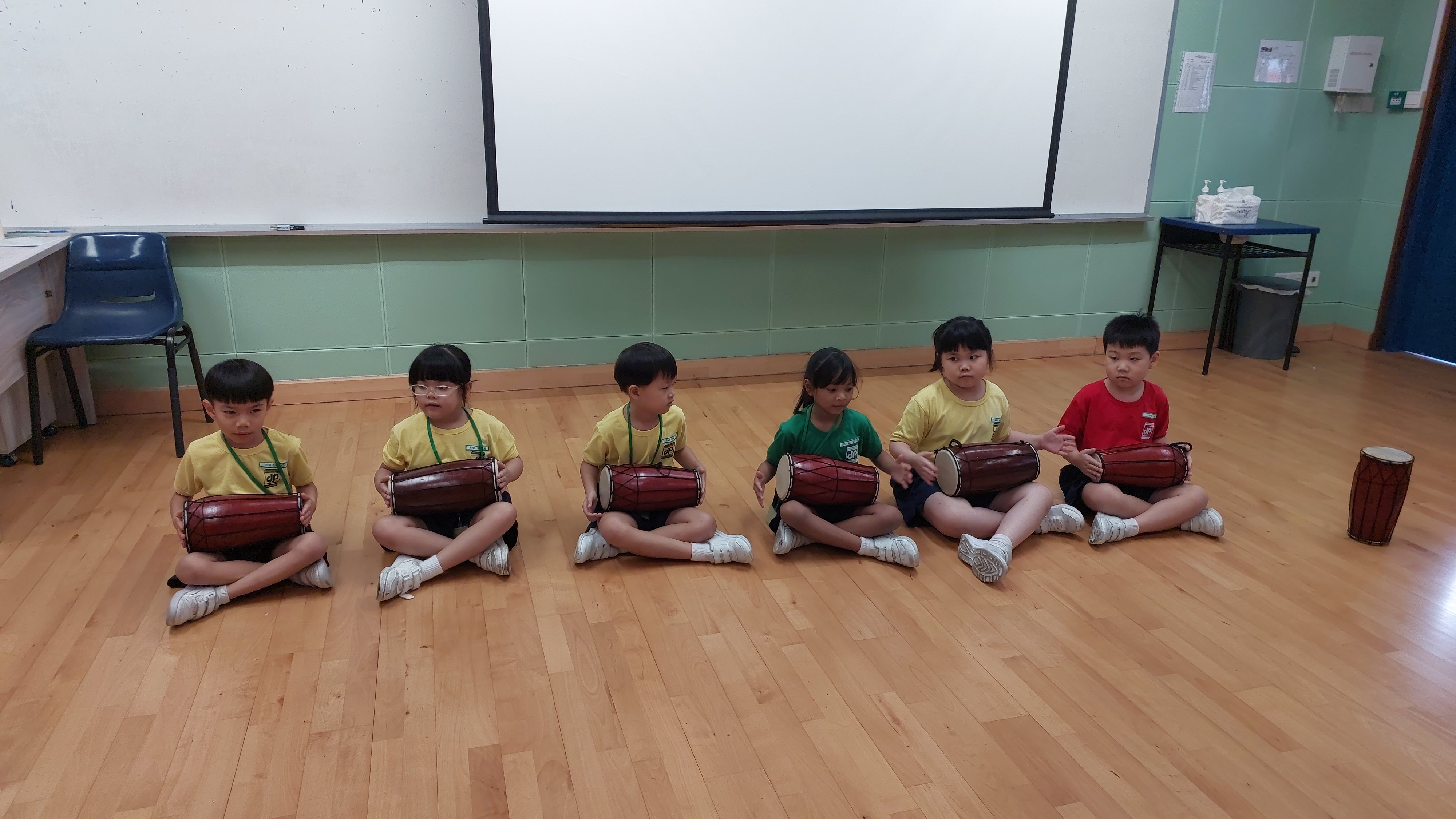 This image shows a group of students sitting in the PAL room playing drum.